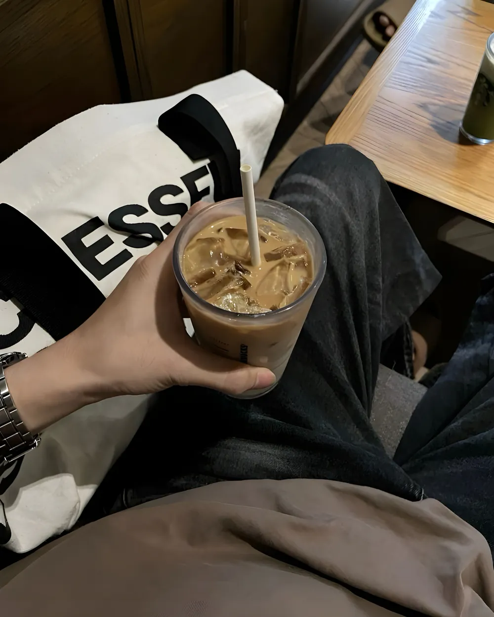 A hand holding an iced milk coffee with a paper straw